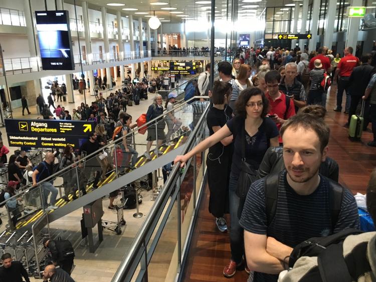 KØ. Passagererne står i en kø, der begynder allerede nede i terminalens ankomsthal og slanger sig i flere lag frem mod sikkerhedskontrollen. 