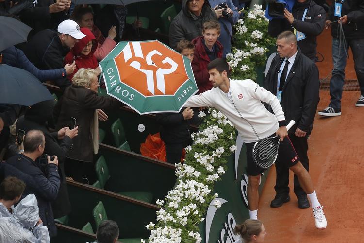 TAK. Novak Djokovic lånte tirsdag en paraply hos en venlig tilskuer på Roland Garros-anlægget i Paris, der stadig mangler et skydetag over hovedbanen. 