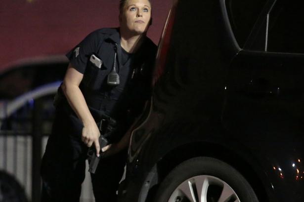 En betjent har søgt dækning bag en bil under skyderiet. 