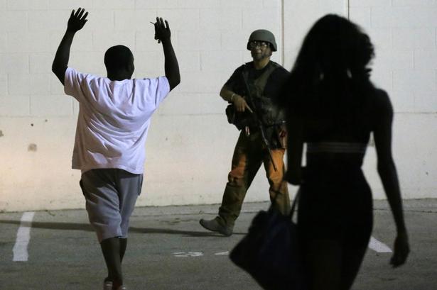 En mand går forsigtigt med armene oppe mod politibejtente i det centrale Dallas. 