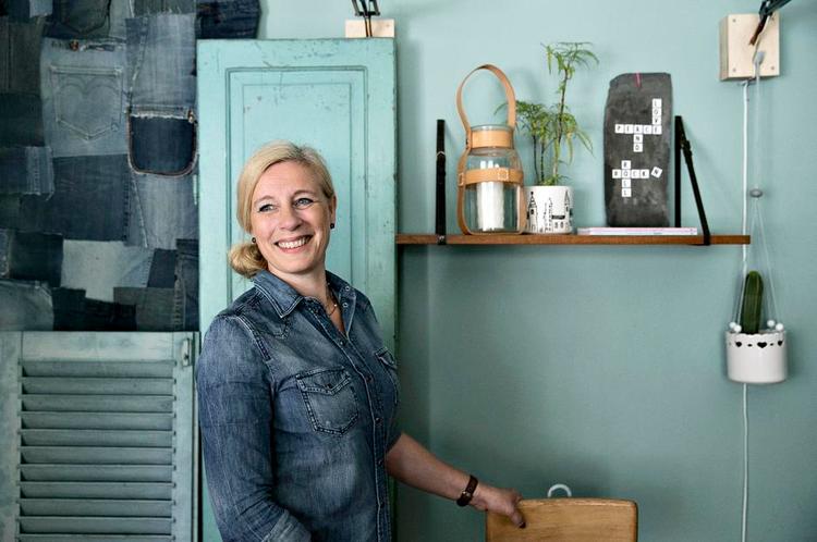 OPHÆNGT. Lene Nissens genbrugshylde i teaktræ er hængt op med slangeskindsbælter. De gamle, hvide potter er hængt op i snører og tegnet på med porcelænstuscher for at give dem nyt liv. Bag hende er et vægtæppe fremstillet af dele af jeans, en gammel køkkenlåge og skodde fra en villa. 