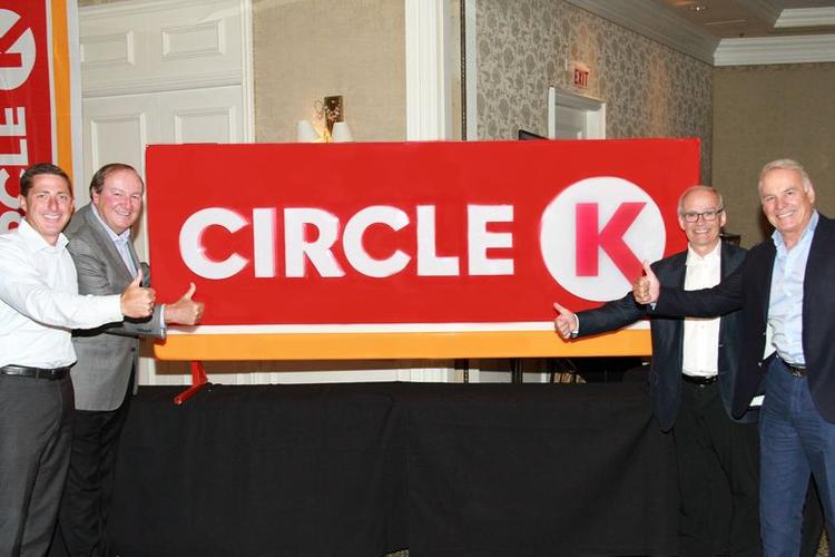 Circlejerk. Her ses cheferne for de canadiske ejere af Statoil, Couche-Tard, posere foran deres nye image-ødelæggende discount-rædselslogo, hvis røde og orange farve er skabt for »at minde om solopgangen – inspirerende hver dag«, som der står i pressematerialet. Om end det ville være mere sandt at skrive »at det føles som at få sand kastet i øjnene hver dag af marketingsfolk«. 