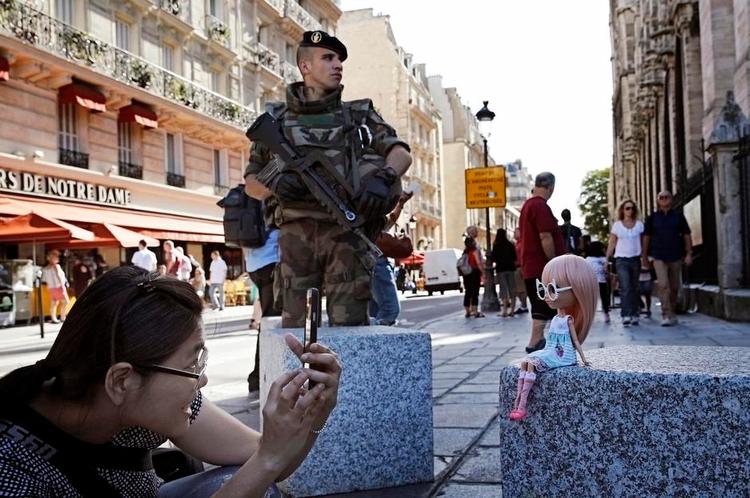 NYE TIDER. En soldat på vagt mod terror ved Notre Dame-katedralen i Paris, mens en turist koncentrerer sig om et billede af sin dukke til minde om ferien i Byernes By. Christophe Ena/AP (Arkivfoto) 