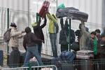 Migranter langer kufferter over hegnet på vej mod de sagsbehandlere, der registrerer 'Junglens' beboere inden flytningen. 