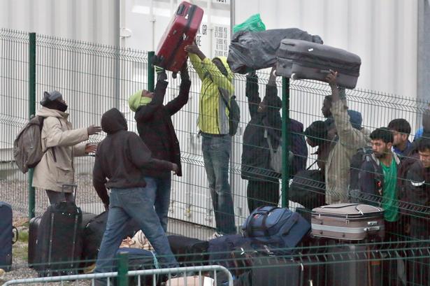 Migranter langer kufferter over hegnet på vej mod de sagsbehandlere, der registrerer 'Junglens' beboere inden flytningen. 