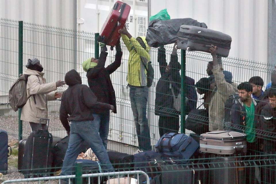 Migranter langer kufferter over hegnet på vej mod de sagsbehandlere, der registrerer 'Junglens' beboere inden flytningen. 