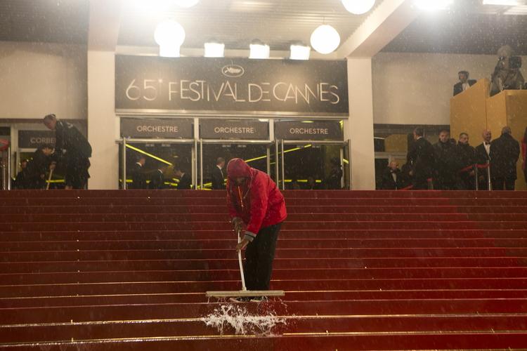 Turen på den røde løber bliver mindre glamourøs end forventet. Fem minutter inden Zentropa ankommer, bliver to Cannes-folk kommanderet ud for at forsøge at fjerne den kæmpe regnpøl, der har samlet sig på toppen af trappen, hvor indgangen til biografen er. Regnen plasker ned, og blæsten flår folks paraplyer i stykker på løberen. Men da filmen er forbi, rejser alle i salen sig og klapper. 