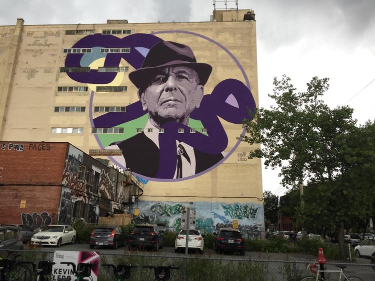 Det er den canadiske kunstner Kevin Ledo, der står bag vægmaleriet af Leonard Cohen, som blev til i forbindelse med vægmalerifestivalen i 2017. Maleriet er knap 40 meter højt.  