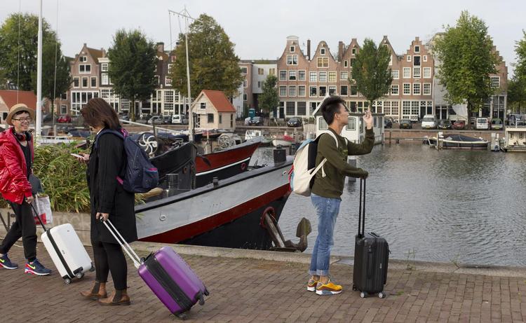 Den rytmiske lyd af rullekufferter og zigzag uden om folk, der er stoppet midt i det hele for at nærstudere et turistkort. Nogle lokale haft fået nok af den massive strøm af turister i Amsterdam og frygter, byen bliver ’disneyficeret’. Foto: Peter Dejong/AP 