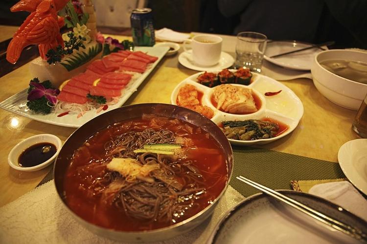 Den nordkoreanske menu består af kimchi, kolde nudler i en chilisuppe, dumplings og et fad med rå laks. 